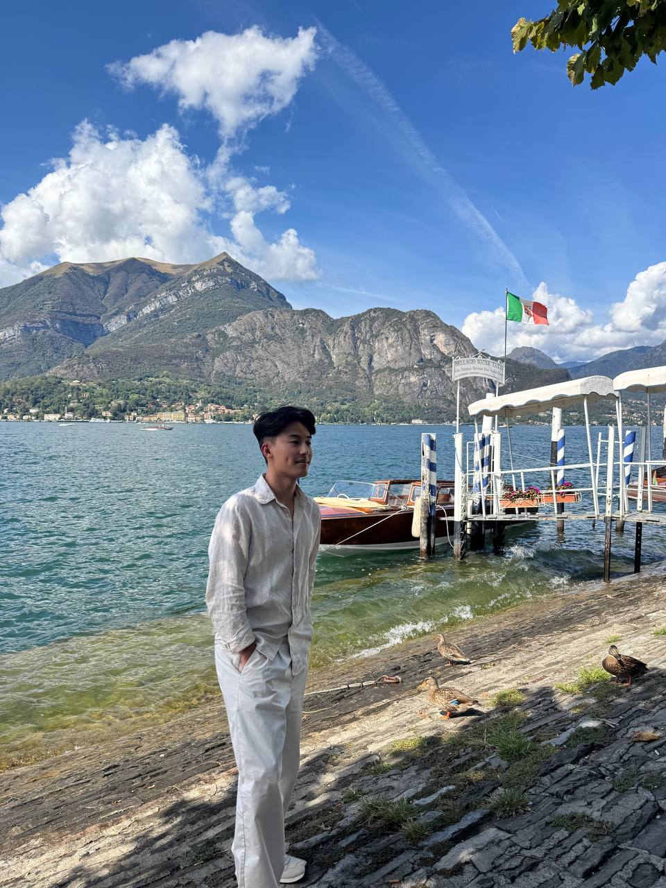 Steven 站在湖畔石岸，旁边是木码头与意大利国旗。